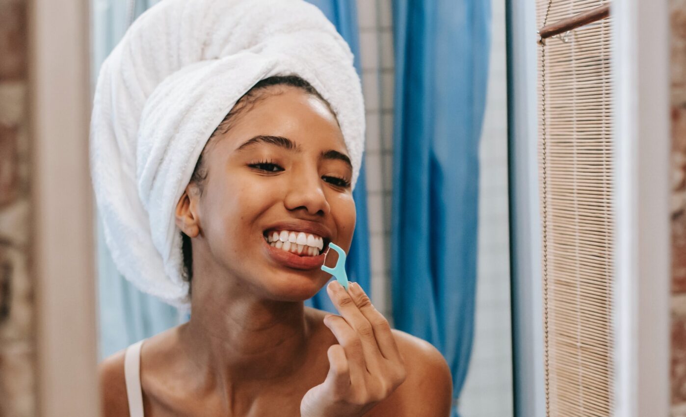 A lady appears happy as she flosses her teeth with a flossing harp