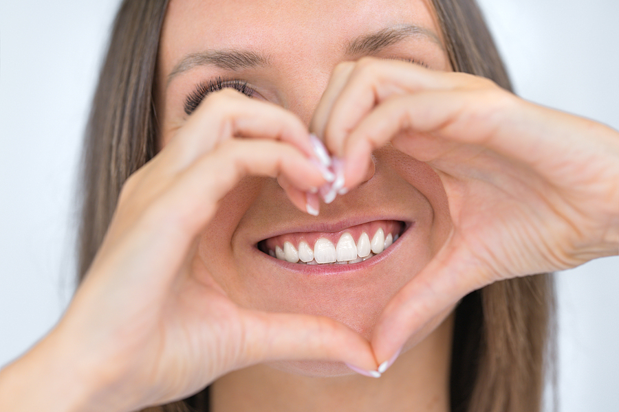 Lady holds hands up to her face in a heart shape. She has white and healthy teeth