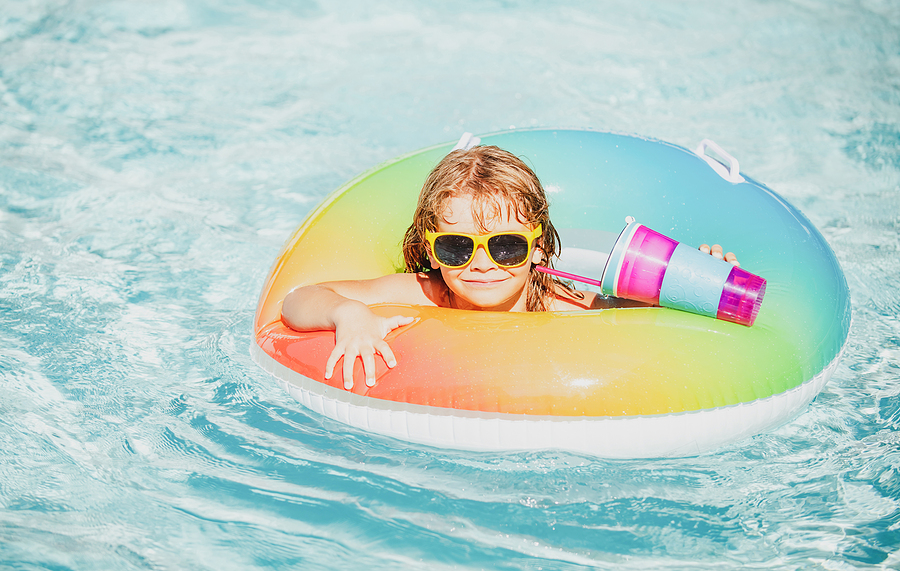 Little girl in rubber ring in swimming pool during summertime 